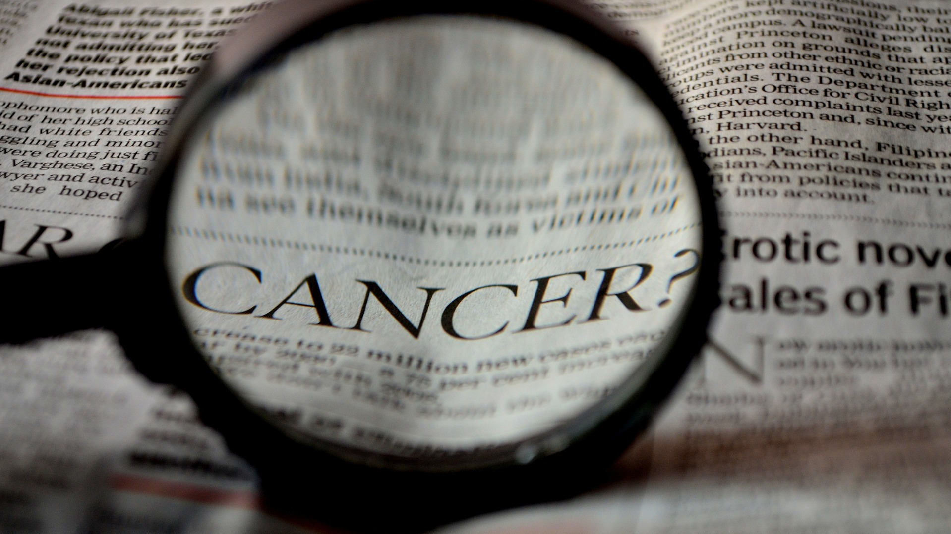 Newspaper and magnifying glass with the word cancer in it