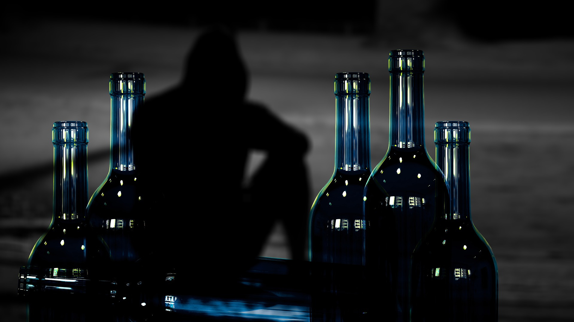 Man sitting in the shadows behind some bottles with alcohol