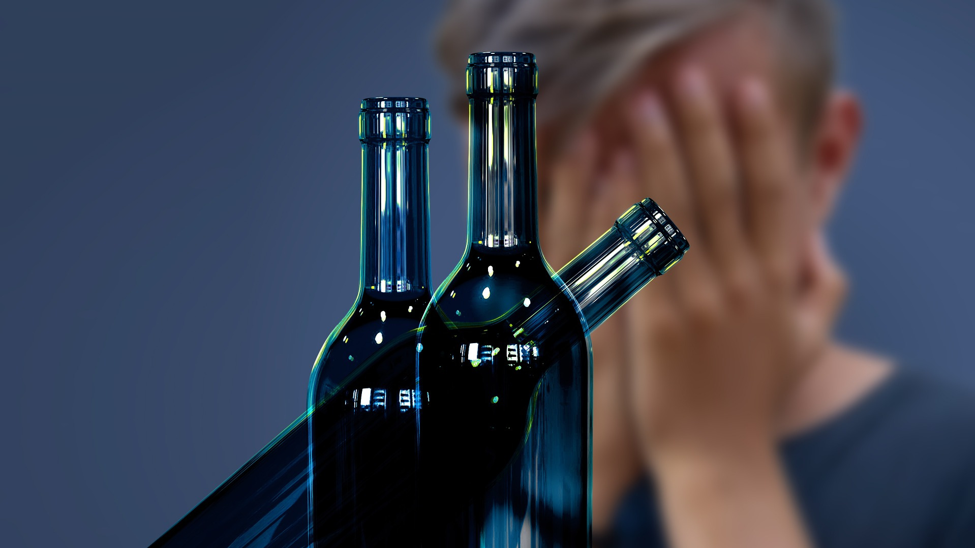 Man with hands covering his face behind bottles of alcolic beverages